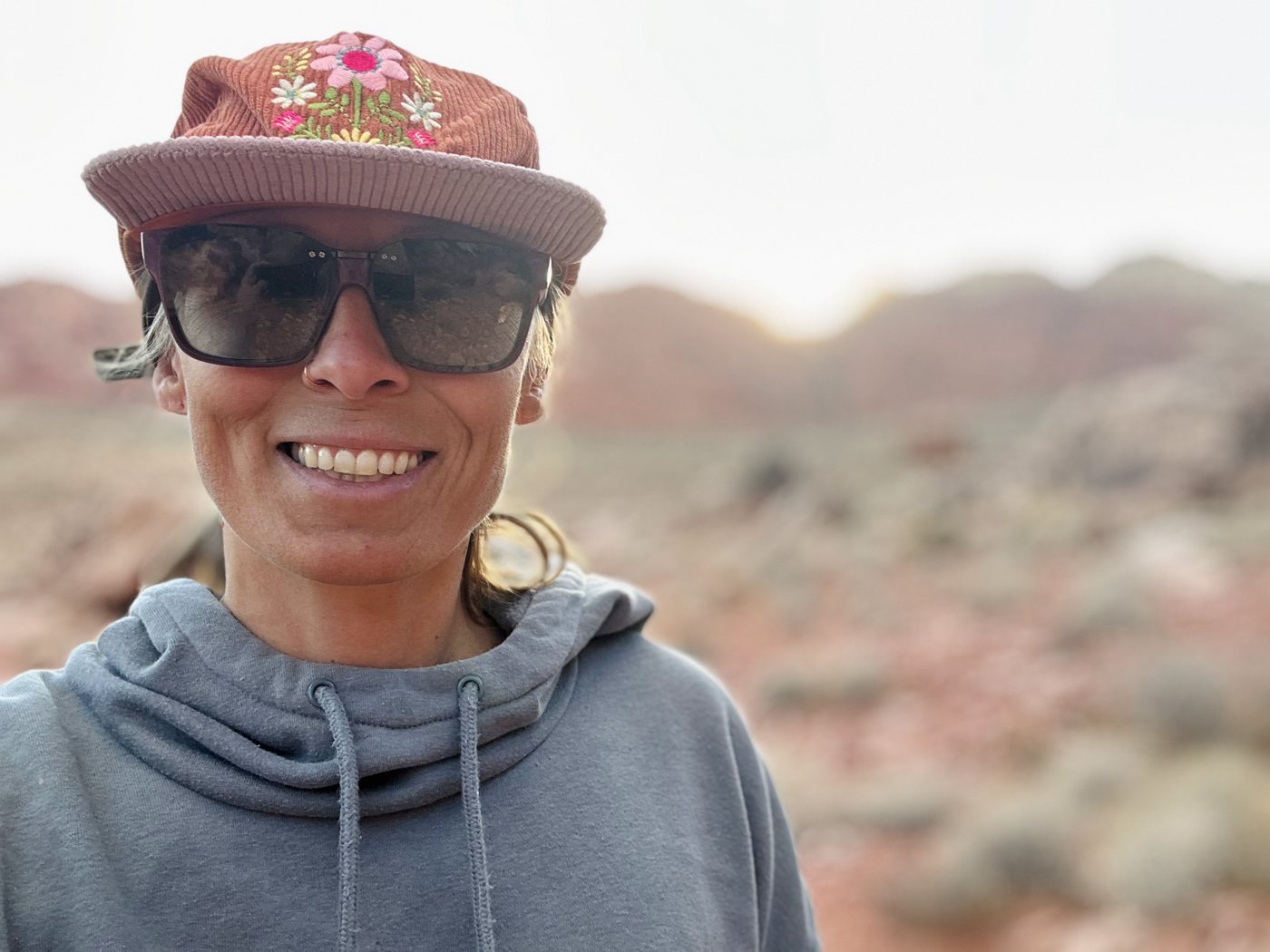 Elise Clausen smiling outdoors in a cap and sunglasses, with red-rock desert behind her